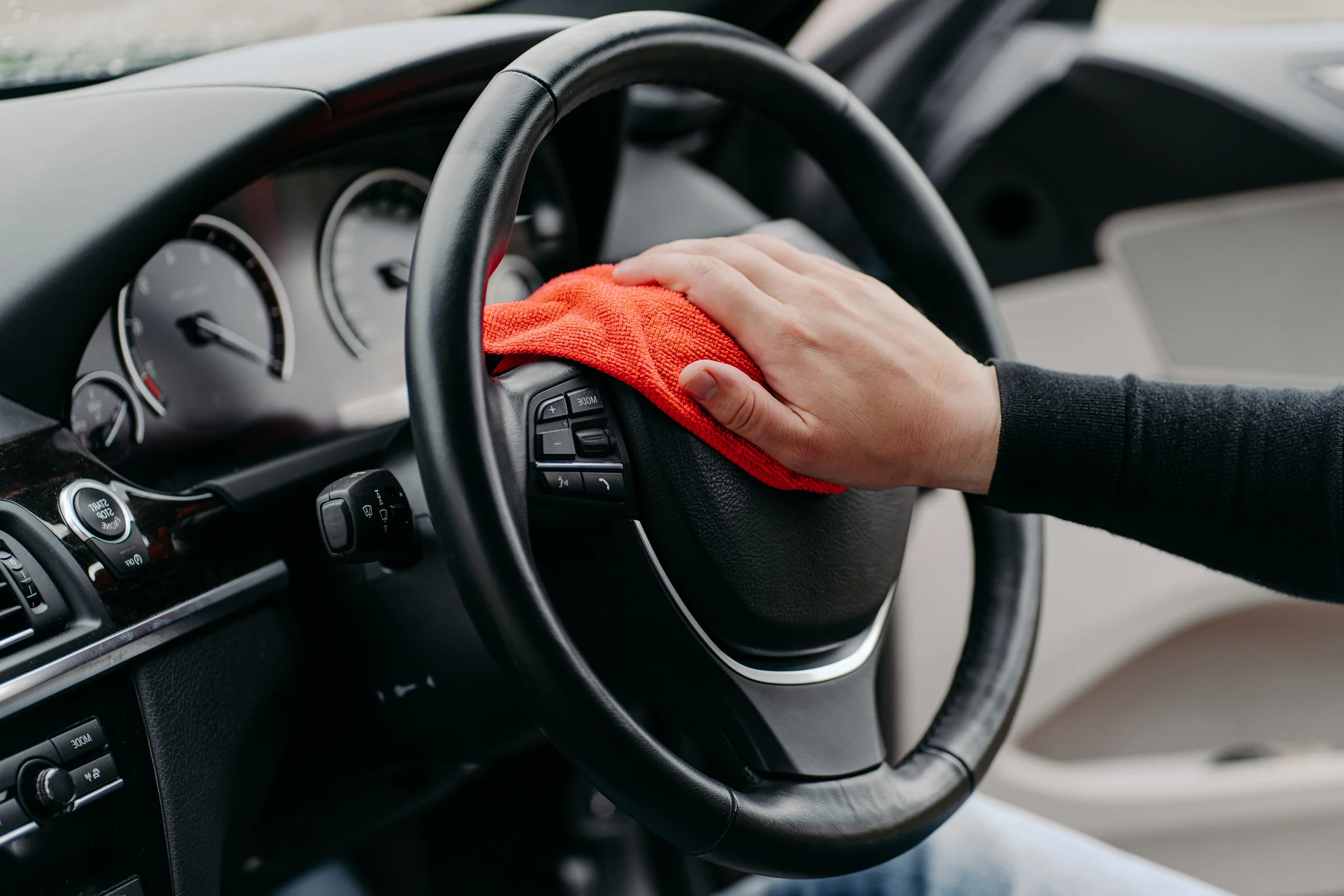 Hand wiping a car steering wheel with a cloth.