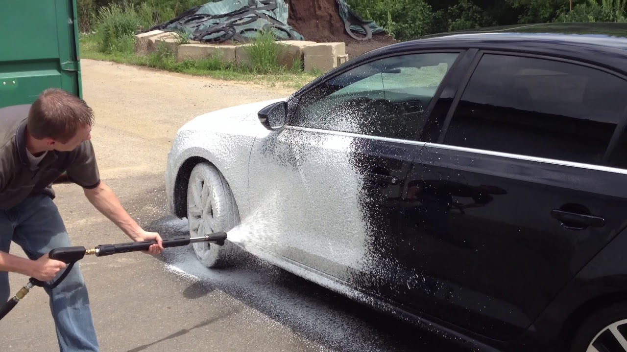 Operator using a pressure washer to foam-clean a car.